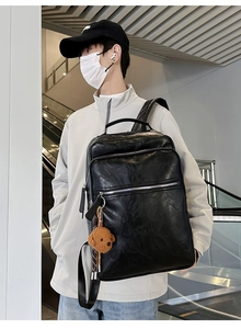 Detail of black faux leather backpack with multiple zippers and plush bear charm