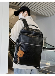 Close-up of black leather backpack with multiple zip pockets and a teddy dog charm