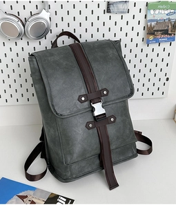 Detail of dark grey leather backpack with brown straps and silver buckles on a desk