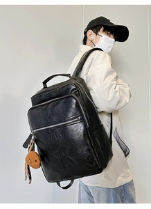 Detail view of large black leather backpack with multi-pockets and a cute bear charm