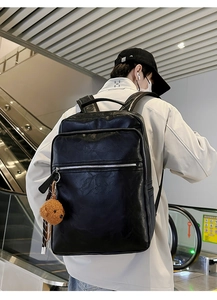 Detail of black vintage faux leather backpack with multiple pockets and a brown bear charm