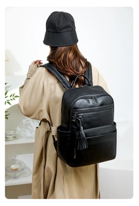 Minimalist black faux leather backpack with metallic zippers and tassel on a model