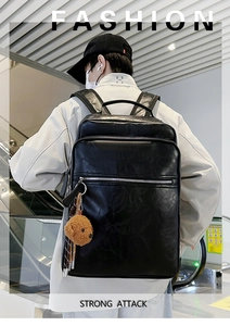 Detail view of black faux leather backpack with multiple zippers and plush bear charm