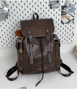Detail of vintage dark brown PU leather backpack with buckle straps and teddy bear charm