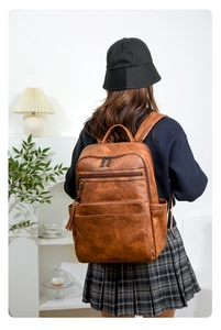 Brown vintage leather backpack with multi-zipper pockets shown on a person in a cozy room