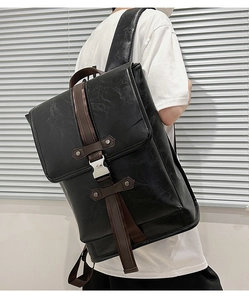 Side view of black faux leather backpack with brown straps on model in front of shutters