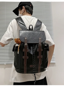 Detail of vintage black men's travel backpack featuring brown leather straps and plush bear charm
