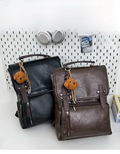 Close-up of retro PU leather backpacks in black and brown with plush dog pendants