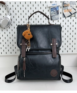 Detailed view of black PU leather backpack with buckle straps and a cute teddy bear pendant
