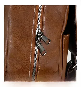 Detail of smooth metal double zippers and white stitching on vintage brown leather backpack