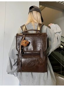Detail of vintage dark brown PU leather backpack with teddy bear pendant and embossed logo