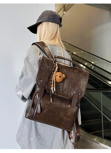 Detail view of brown vintage PU leather backpack with buckle straps and plush bear charm