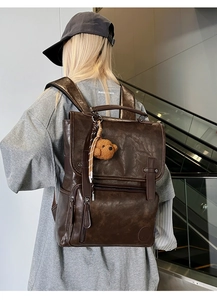 Detailed close-up of brown PU leather backpack with vintage buckle and bear charm