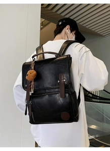 Detail of a black PU leather backpack featuring brown straps and a cute plush bear charm
