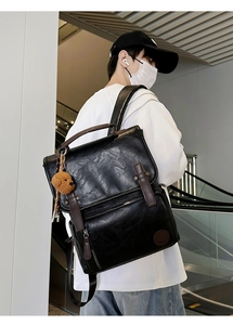 Rear view of a black pebble leather backpack with brown trim on a male model outdoors