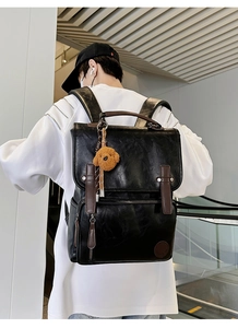 Detail of black pebbled leather backpack with brown trim and cute bear charm accent