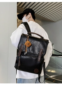 Detail of black PU leather backpack with buckle straps and brown bear plush charm