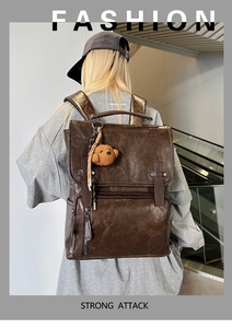 Detail of dark brown vintage PU leather backpack with decorative straps and bear charm