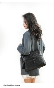 Model wearing black washed leather crossbody bag with multiple zippers and tassel detail
