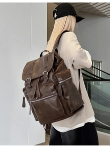 Detailed view of the vintage brown leather backpack showing buckled flap and zip pockets