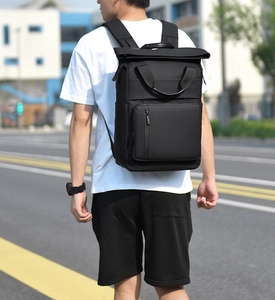 Rear view of model wearing a black roll-top business laptop backpack on city street