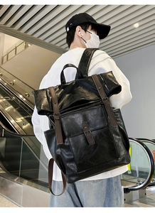 Urban commuter black leather backpack with brown strap buckles on a person at an escalator