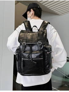 Man wearing a large black PU leather backpack with buckle straps in a modern interior