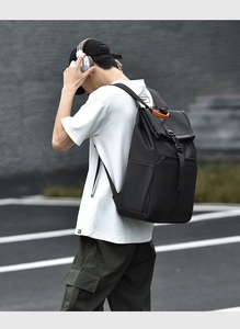 Detail of black roll-top backpack with orange handle accents on a male model