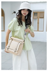 Detail of beige bucket bag featuring geometric woven strap and front buckle pocket