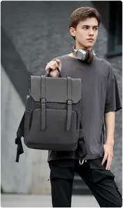 Outdoor shot of a man holding a dark grey functional backpack with buckle and zipper detail