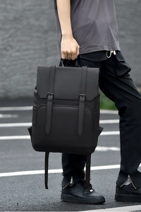 Side view of black minimalist buckle backpack in matte material on city street