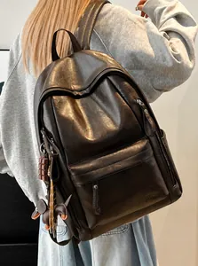 Detalle de mochila de cuero marrón oscuro con logotipo grabado y colgante decorativo