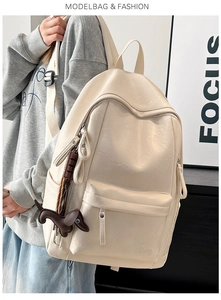 Detalle de una mochila beige de cuero sintético con un dije de perro marrón y bolsillos