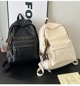 Close-up of soft leather backpacks in black and beige with cute dog pendant and textured finish