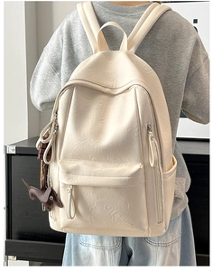 Detalle del bolso de cuero crema con textura granulada y colgantes decorativos
