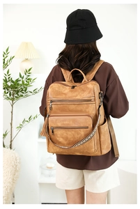 Detail of vintage brown leather backpack featuring multiple zippers and ethnic woven strap