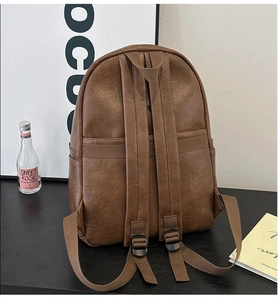 Rear view of dark brown leather backpack with adjustable straps on a black table