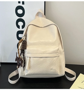 Detail of cream white leather backpack featuring a side dog charm and front zipper pocket