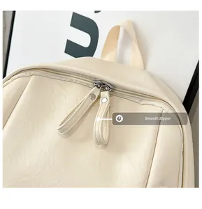 Detalle de cremalleras plateadas y textura de cuero PU crema en una mochila escolar
