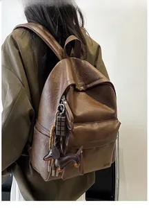 Detail of soft brown leather backpack featuring a cute dog charm and metallic zipper