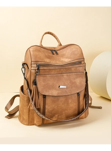 Detail view of tan PU leather backpack with tassel charm and woven shoulder strap