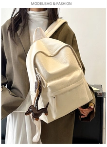 Detail of soft cream PU leather backpack with minimalist logo and dog charm on shoulder