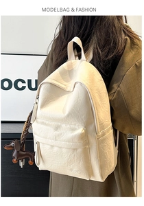 Detail of cream leather backpack featuring soft pleated texture and dog-shaped charm