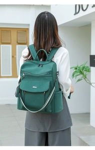 Close-up of dark green backpack with multi-layer zippers and stylish fringe pendant