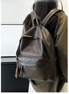 Detail of soft brown leather backpack featuring a front zipper pocket and embossed logo