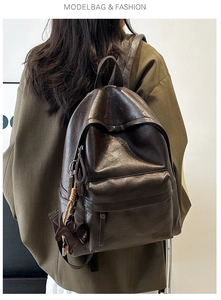 Detail of dark brown leather backpack with rabbit charm worn by a model on plain background
