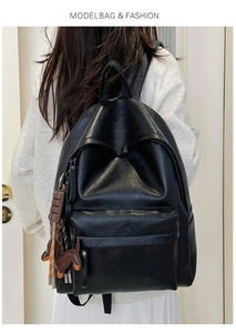 Detail view of black soft leather backpack with zipper pockets and cute puppy pendant accessory