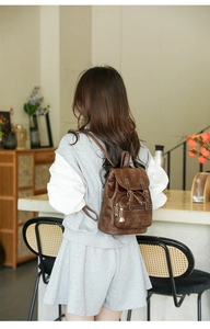 Close-up of vintage brown PU leather backpack with gold zipper on a model in a cafe
