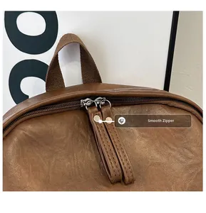 Detail view of smooth metal double zippers and leather pulls on a brown leather backpack