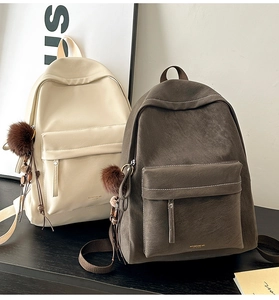 Detailed close-up of beige and brown leather backpacks with plush charm and zipper pocket